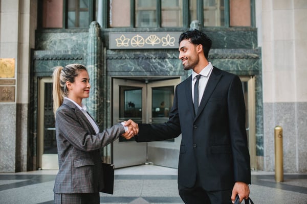 Two employees shaking hands in front of building