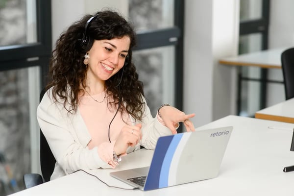 Lady sitting at a table with headset talking into a laptop and smiling