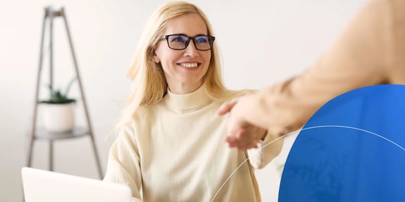 Woman wearing glasses shaking hands with another person and smiling