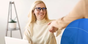 Woman wearing glasses shaking hands with another person and smiling