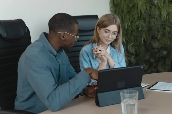 Two employees sitting at desk looking into tablet and discussing