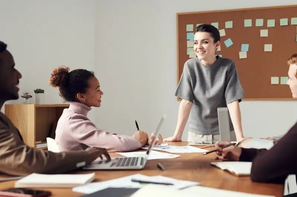 Woman standing infront of desk with other employees smiling and talking