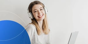 Woman wearing white headphones smiling at camera holding lapotp 