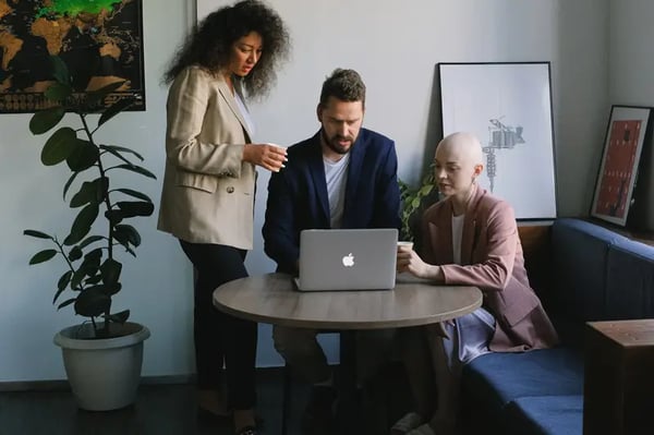 Two female and one male employee around desk looking into laptop