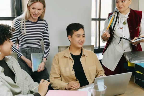 Four employees gathered around desk talking and smiling with each other