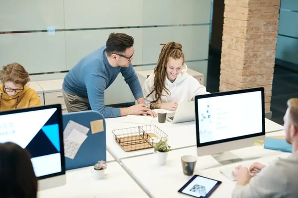 2 employees at desk smliling and looking into laptop screen