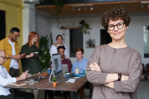 Woman standing with arms crossed and smiling at camera with employees in background