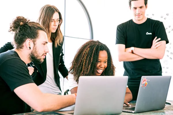 Four employees sitting around desk into looking laptop screen and smiling 