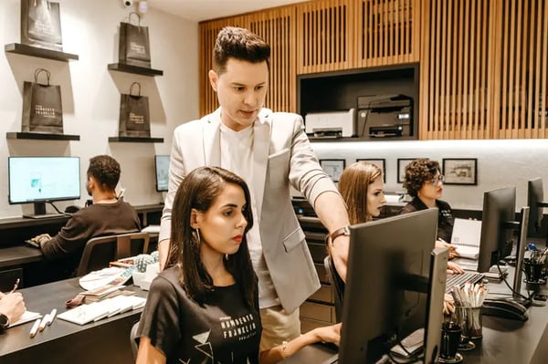 A male employee standing behind female employee who is sitting and pointing at computer screen