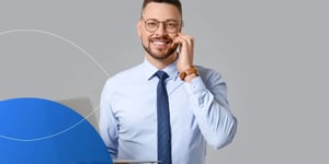 Man wearing glasses and holding a phone to his ear as he smiles into the camera 