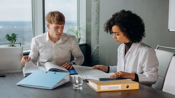 Two employees sitting at desk looking through files