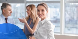 Woman sitting at desk and smiling to camera with another woman and man in the background