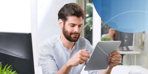 man sitting at desk scrolling on tablet