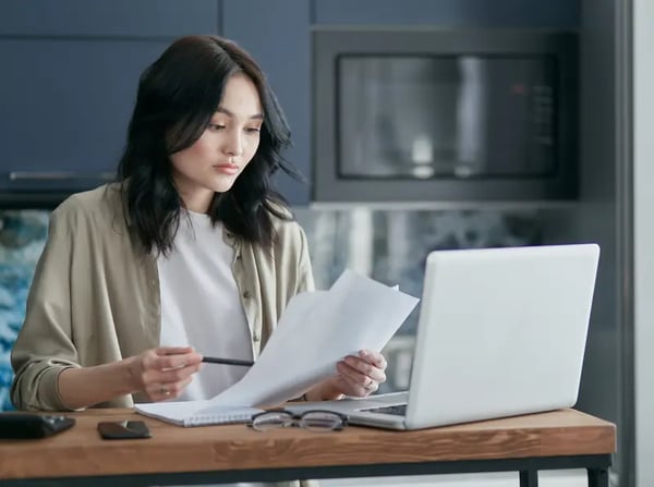 Female looking at papers sitting on desk with laptop 