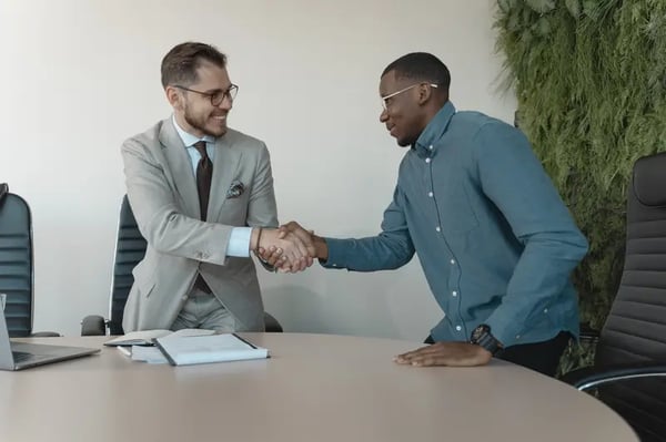 Two men in meeting room shaking hands across table and smiling