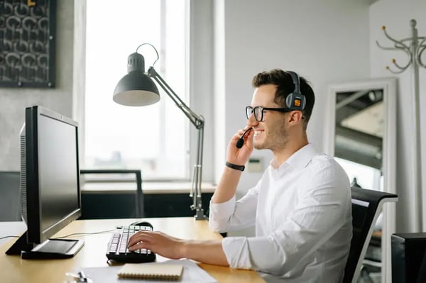 Man looking at a computer monitor while wearing a headset, smiling.