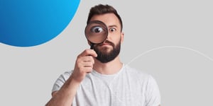  man holding magnifying glass up to one eye and looking to camera 