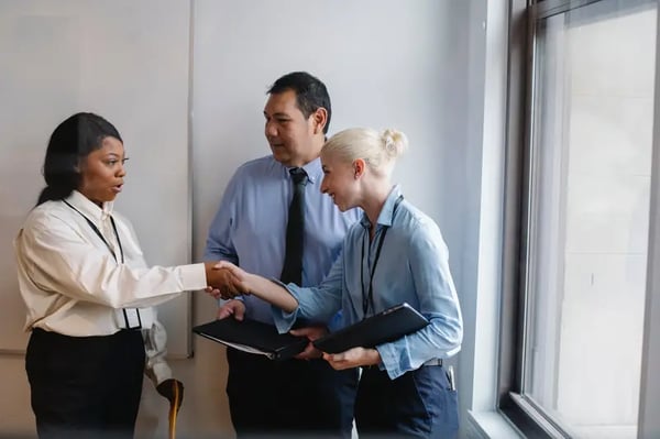 Two female employees shaking hands in front of male employee
