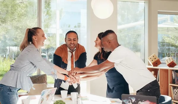 group of employees standing around the table with their hands together in the middle