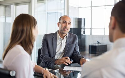 A manager answering a question across a meeting table from two colleagues