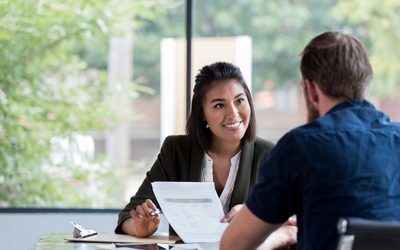 A rep and a customer talking across a desk, the rep holding a printed offer