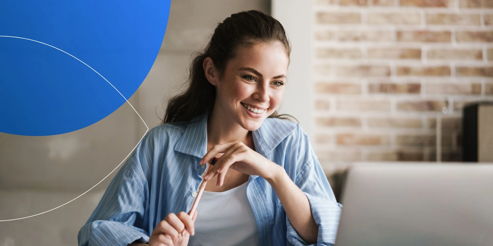 woman holding pen and smiling into laptop 