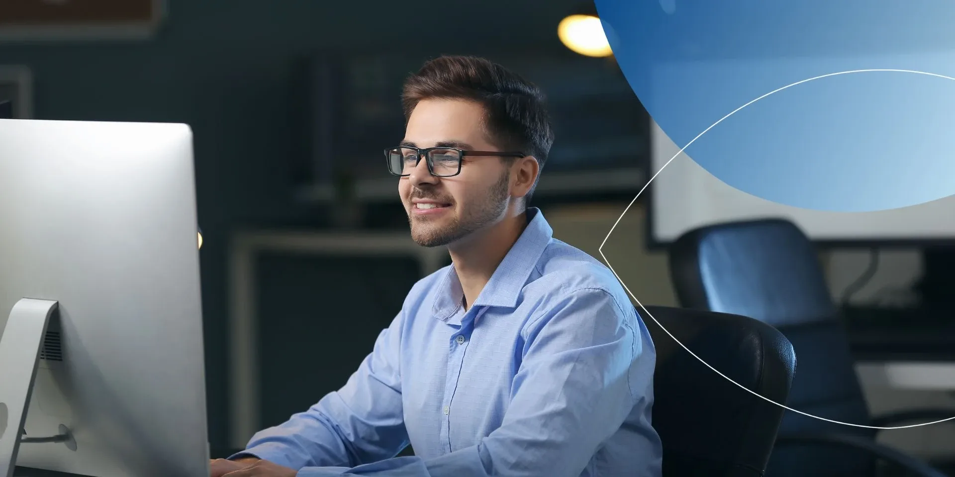Man wearing glasses sitting on desk and smiling at computer screen 