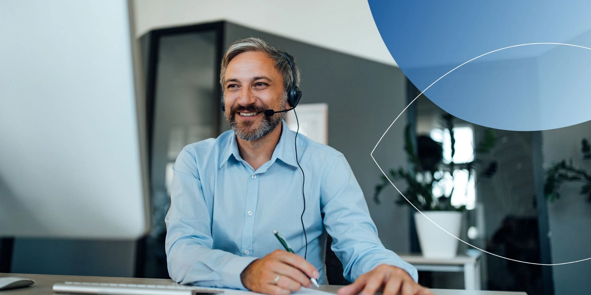 man wearing headsets holding a pen and smiling into computer screen